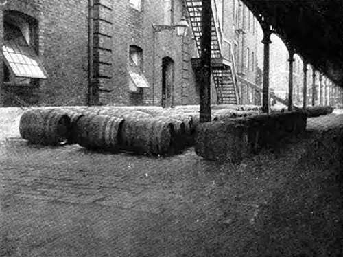 BARRELS OF RUM ON THE WHARF AWAITING SHIPMENT.