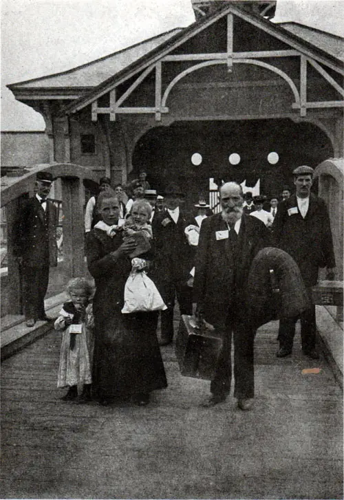 AT THE GATE With tickets fastened to coats and dresses, the immigrants pass out through the gate to enter into their new inheritance, and become our fellow citizens.