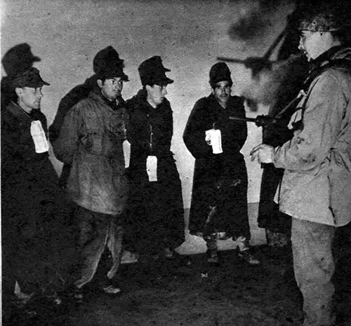 Pvt. Hubert Campbell of Eugene, Oreg., a 10th Division MP, stands guard over a bunch of prisoners