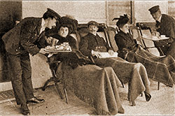 First Class Passenger Enjoy the Luxury of Relaxing on a Steamer Chair Covered With a Steamer Rug To Keep Them Warm and Cozy While Being Served Sandwiches by the Steward.