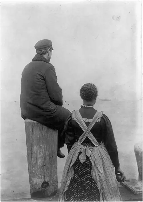 Two Immigrants on a Dock Facing the Water at Ellis Island.