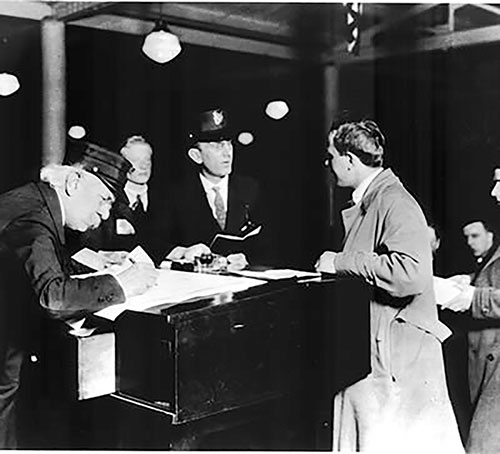 Immigrant Man is Questioned by Inspector at the Registry Desk While a Clerk Records Notes on the Passenger Manifest.