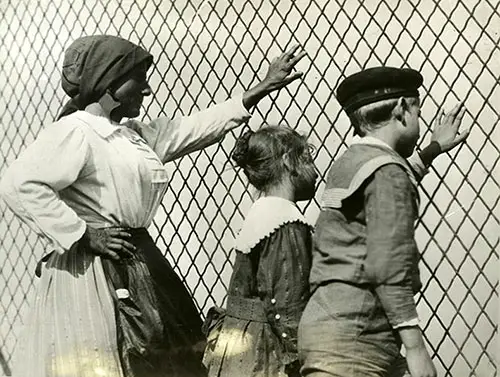 A Woman, Girl and a Boy Pearing Out Against a Chain Link Fence at Ellis Island.