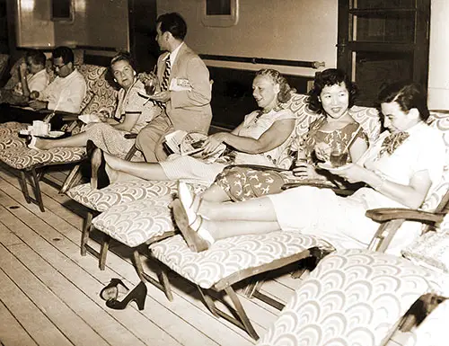 Passengers Sitting on the Promenade Deck of the RMS Caronia on Deck Lounge Chairs, Drinking, Chatting, and Reading, February 1951.