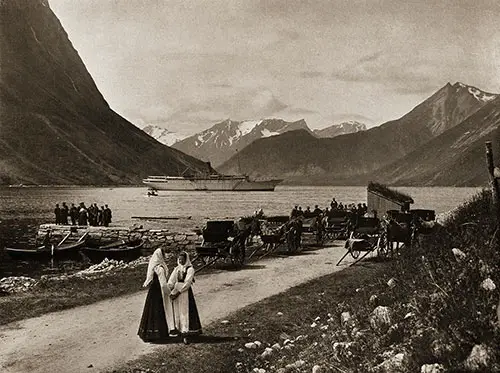 Two Women in Foreground Wearing Traditional Norwegian Folk Costumes. The SS Meteor in the Background is Near Oie Nordangsfjorden.