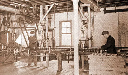 Fig. 4 - The Weighing Machines, Supplied by the Inclined Spouts From Feed Bins in the Fourth Story, Fill the Tins Which Are Carried by the Conveyor To the Vacuum Sealer at the Left.